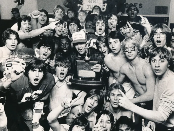 A lively group of young people celebrating around a trophy.